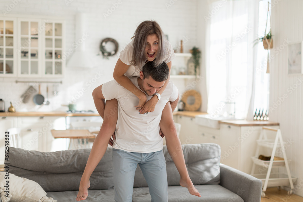 Spending time at home. Happy couple spending time together enjoying piggyback in light kitchen. Spending time at home. Happy couple spending time together enjoying piggyback in light kitchen.