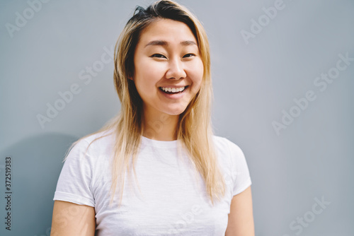 Cropped image of pretty asian female person standing against wall with copy space for your advertising content.Half length portrait of cute hipster girl looking at camera while spending time outdoors photo