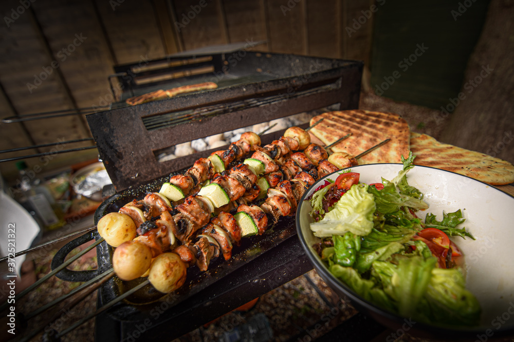 Freshly grilled meat and vegetable skewers with salad and flat bread on outdoor barbecue