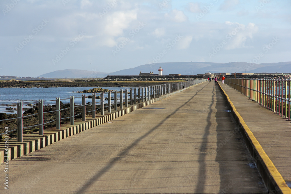 Asphalt road to the lighthouse with railings and the sea next to Galway