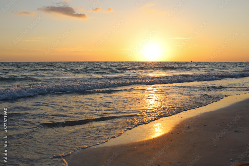 Sunset illuminates tranquil waves and shoreline along the beach in Lido Key off Sarasota, Florida. Glowing yellow sun sets over calm Gulf of Mexico waters near Siesta Key. Summer nights in FL.