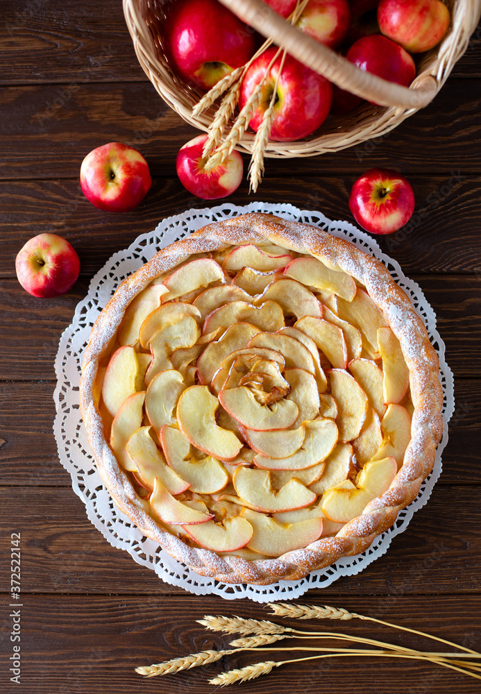 Round apple pie and red apples on brown background