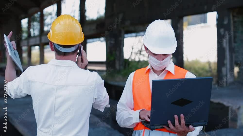 Workers in masks use phone and internet communications in the demolition building. Rebuild and reimagine jobs amid the coronavirus crisis, support enterprises and workers during restructuring. Workers in masks use phone and internet communications in the demolition building. Rebuild and reimagine jobs amid the coronavirus crisis, support enterprises and workers during restructuring.