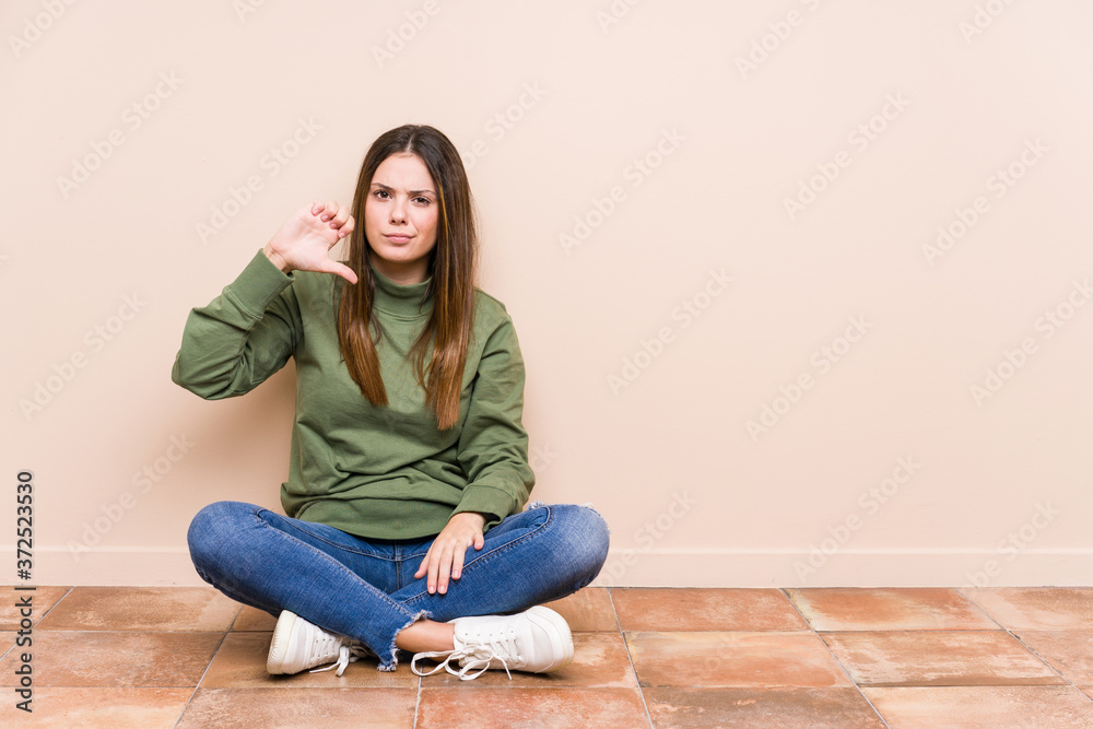 Young caucasian woman sitting on the floor isolated showing a dislike gesture, thumbs down. Disagreement concept.