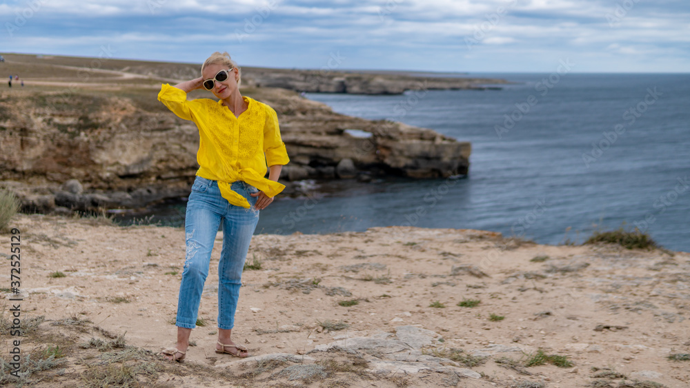 Cheerful lady in a yellow shirt with a lovely smile on blue clouds in hot sunny weather on a cliff Cheerful lady in a yellow shirt with a lovely smile on blue clouds in hot sunny weather on a cliff