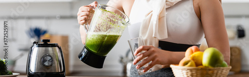 panoramic crop of young woman holding blender with mixed smoothie near glass
