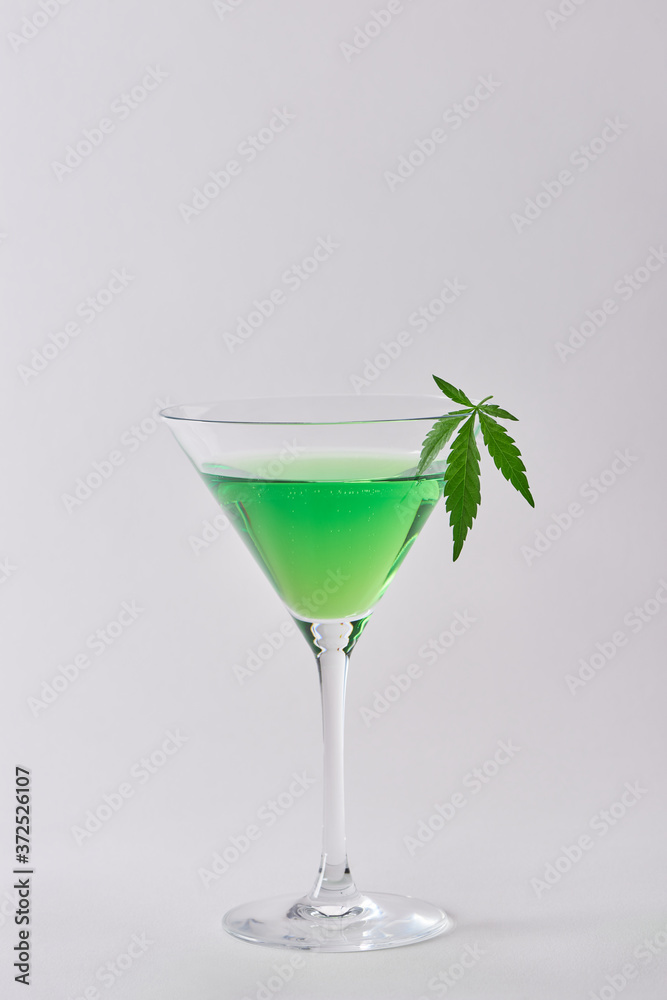 A glass of green cocktail with cannabis infusion on white background