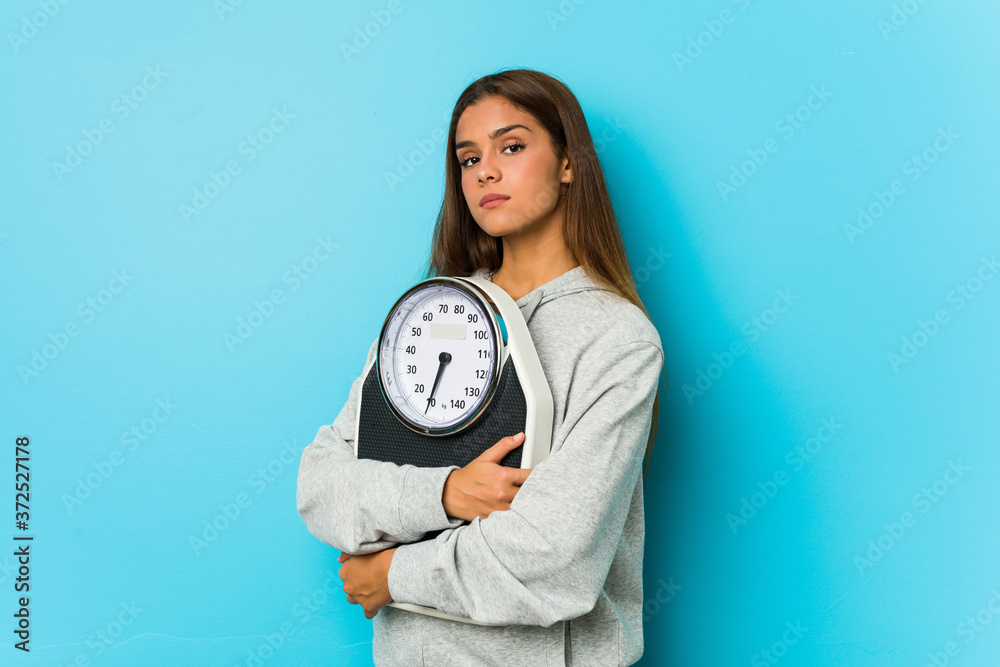 Young caucasian woman holding a scale isolated on a blue background Young caucasian woman holding a scale isolated on a blue background