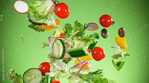 Flying vegetable salad isolated on green background. Healthy eating and lifestyle.