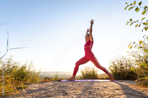 Beautiful lady in sporty top and shorts practicing yoga with amazing sunshine view on background