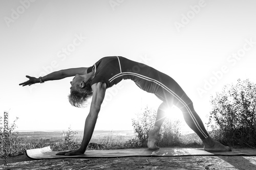 Black and White Old Woman in red Tracksuit try doing Wheel half Moon power Pose one hand in the sunrise