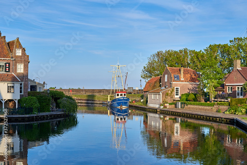 Malerische Ansicht mit Wasserspiegelungen und alten historischen Gebäuden in Enkhuizen am Ijsselmeer in den Niederlanden, mit Blick auf den Kanal zum Hafen Oosterhaven in dem ein Fischerboot liegt. photo