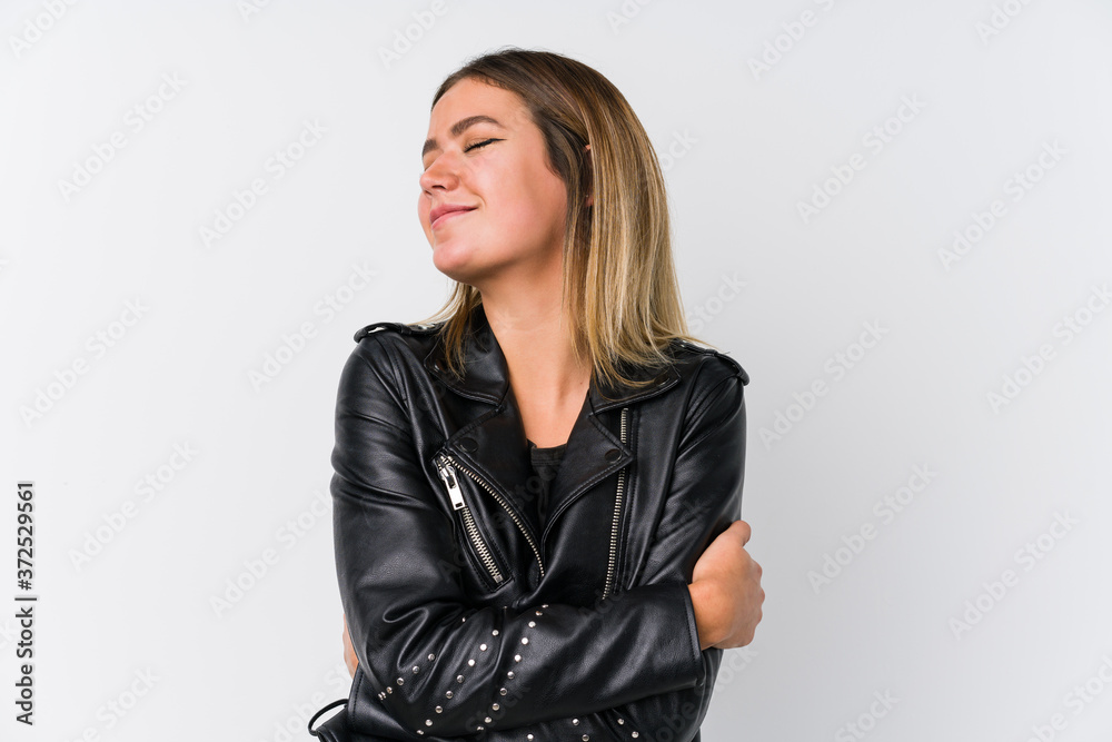 Young caucasian woman wearing a black leather jacket hugs, smiling carefree and happy.