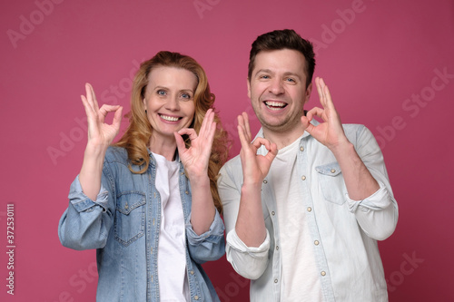 Good looking smiling man and woman showing OK sign with two hands. Positive facial human emotion. Studio shot