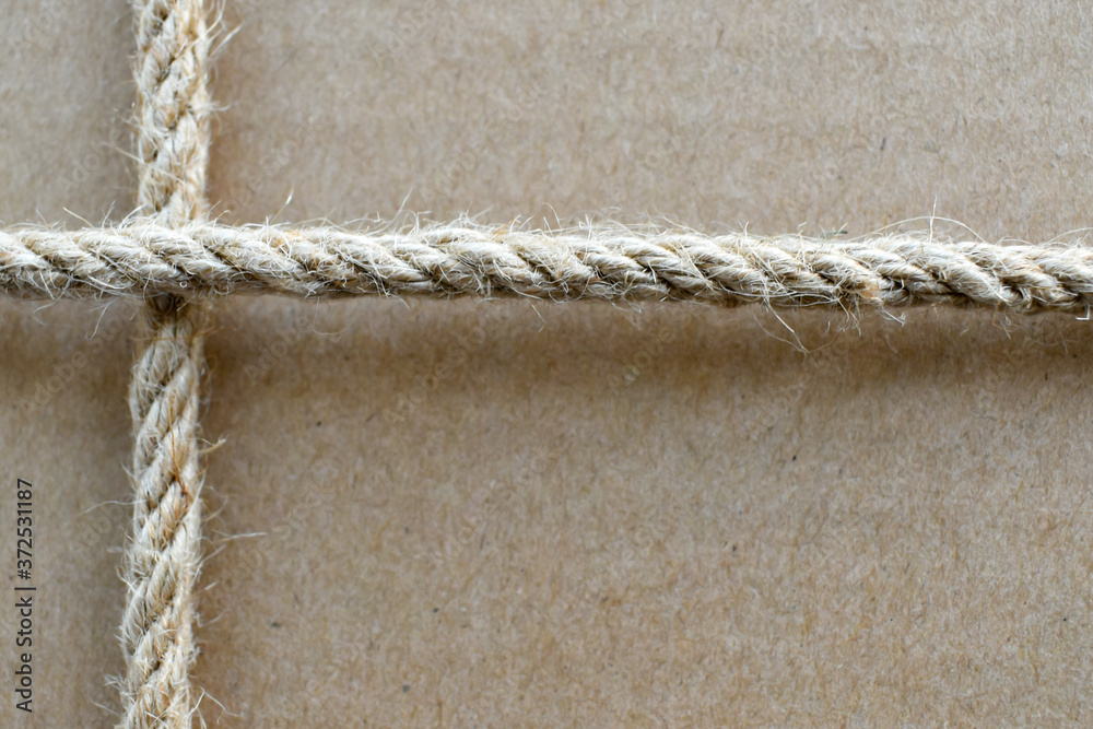 Craft paper box tied with jute rope criss-cross. Close-up. Brown textured background with rope frame. Gift close-up. grainy texture of cardboard box background. Craft paper box tied with jute rope criss-cross. Close-up. Brown textured background with rope frame. Gift close-up. grainy texture of cardboard box background.