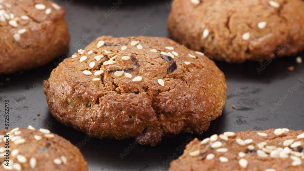 Oatmeal cookies with sesame seeds close-up on a black background moving from right to left. Oatmeal cookies with sesame seeds close-up on a black background moving from right to left.
