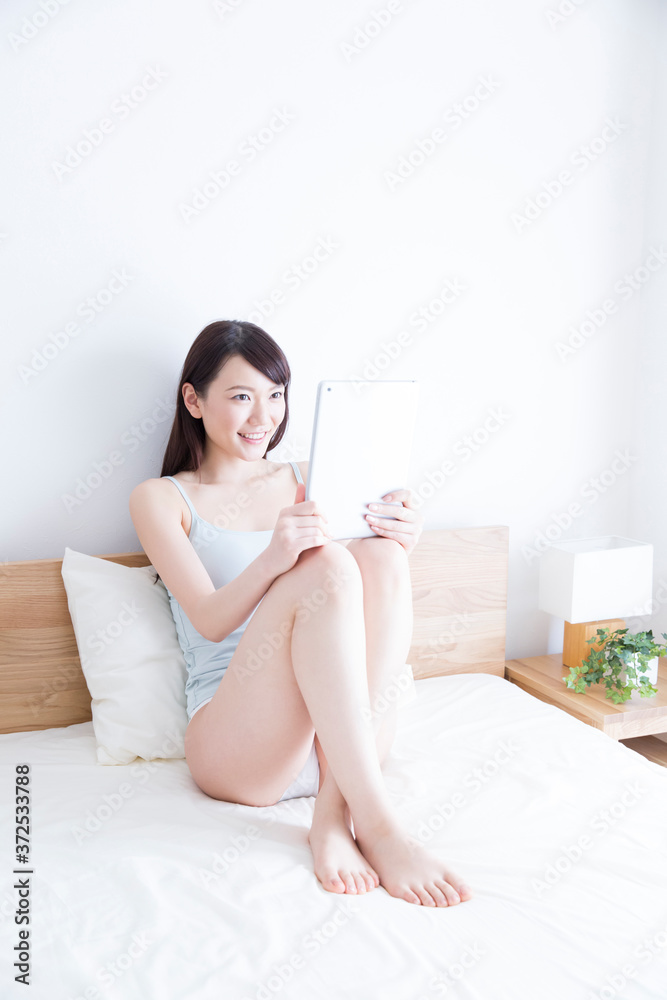 ベッドでタブレットPCを見る女性 ベッドでタブレットPCを見る女性