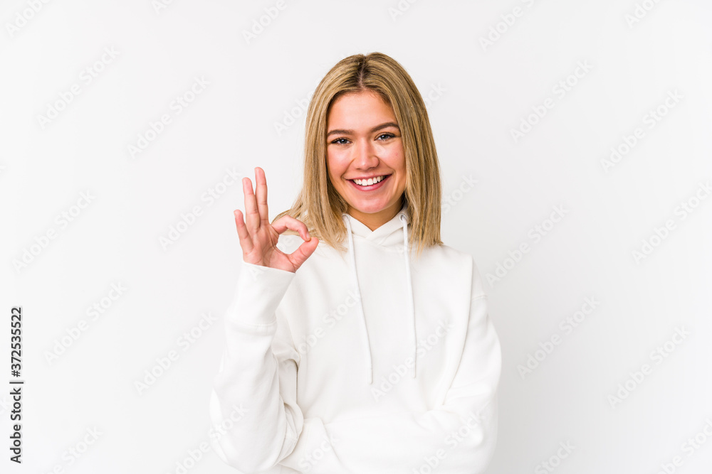 Young blonde caucasian woman isolated winks an eye and holds an okay gesture with hand. Young blonde caucasian woman isolated winks an eye and holds an okay gesture with hand.