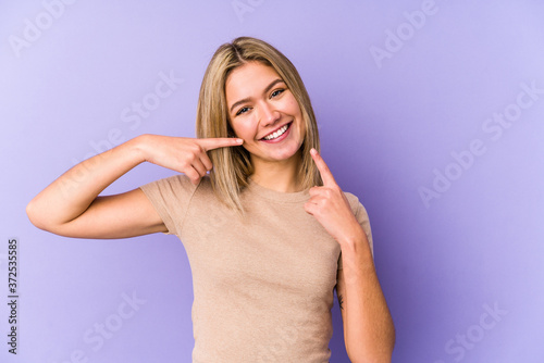 Young blonde caucasian woman isolated smiles, pointing fingers at mouth.