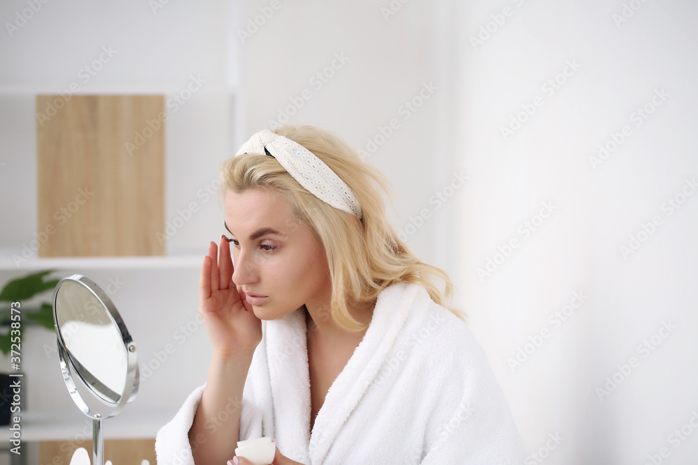 Morning care, a young girl in a bathrobe and with a white towel uses body cream.