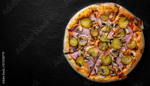 Pizza with Mozzarella cheese, ham, tomato sauce, pepper, pickled cucumbers and mushrooms. Italian pizza on Dark grey black slate background