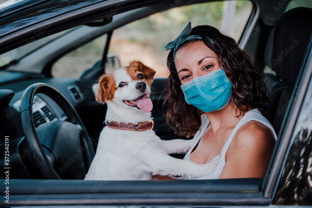 young woman wearing protective mask in a car. cute jack russell dog besides. Travel and new normal concept