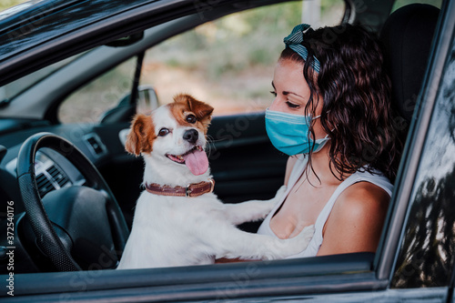 young woman wearing protective mask in a car. cute jack russell dog besides. Travel and new normal concept © Eva