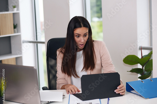 Happy businesswoman with raised so hand gesture reading letter on desk in front of laptop. The businessman is satisfied with the good news from the correspondence.