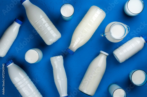 Collection of bottles and glasses with milk on blue background, top view