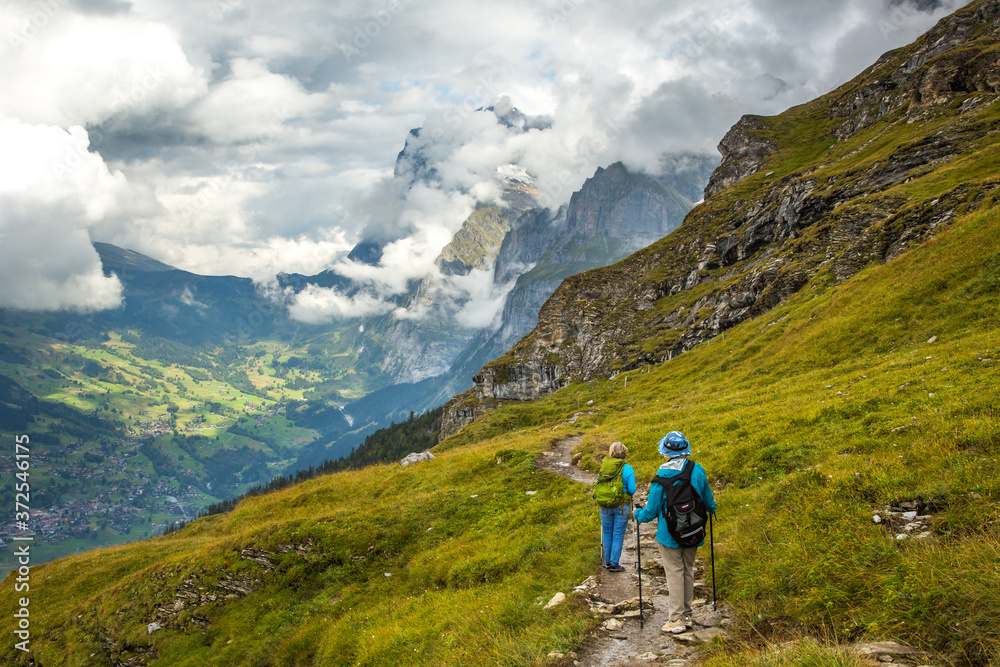 Two women hikers on the Eiger trail in the Alps mountains above Lauterbrunnen, Switzerland.  The village of Grindelwald is in the background.