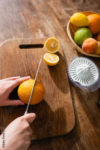 cropped view of woman cutting orange near juicer