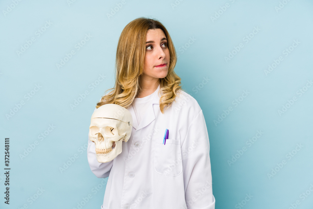 Young doctor woman holding a skull isolated confused, feels doubtful and unsure. Young doctor woman holding a skull isolated confused, feels doubtful and unsure.