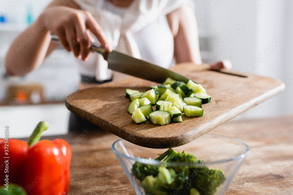 cropped view of woman holding cutting board with sliced cucumber near bowl with broccoli cropped view of woman holding cutting board with sliced cucumber near bowl with broccoli