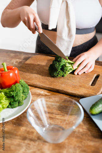 Fototapeta Naklejka Na Ścianę i Meble -  cropped view of woman cutting fresh broccoli on chopping board near vegetables