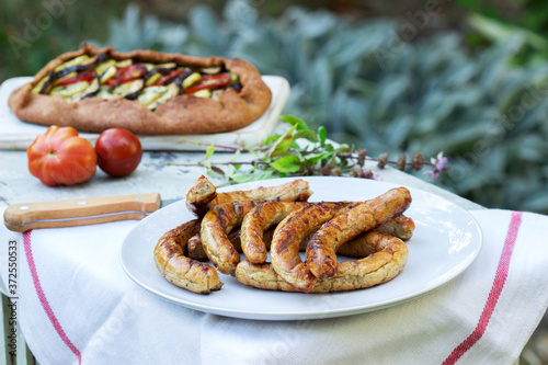 Sausages and vegetarian pies with vegetables and herbs on a wooden table in the garden. Rustic style.