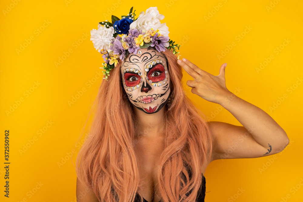Unhappy blonde young female imitates gun shoot makes suicide gesture keeps two fingers on temples has puzzled expression dressed in casual clothes stands indoors. Unhappy blonde young female imitates gun shoot makes suicide gesture keeps two fingers on temples has puzzled expression dressed in casual clothes stands indoors.
