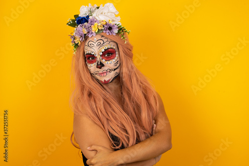 Image of cheerful pretty young caucasian woman wearing halloween make up standing indoors with arms crossed. Looking and smiling at the camera. Confident girl.