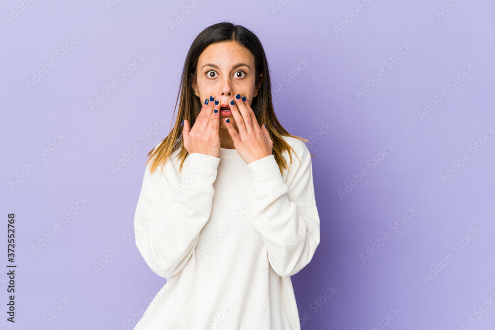 Young woman isolated on purple background shocked covering mouth with hands. Young woman isolated on purple background shocked covering mouth with hands.