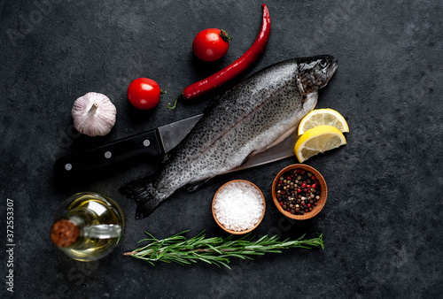 Raw fish trout with spices and ingredients on a knife on a stone background