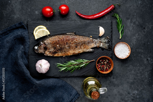 Fried fish trout with spices and ingredients on stone background