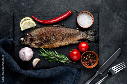 Fried fish trout with spices and ingredients on stone background