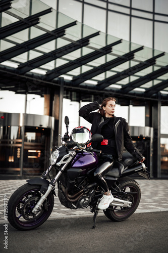 Cool girl in a motorcycle jacket sits with a motorcycle helmet on a motorbike