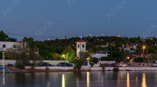 Salamina, Greece - August 16, 2020: Landscape view of a coastal road in Salamina island Greece with light reflection on the sea water. Full of green trees hill view in the background..