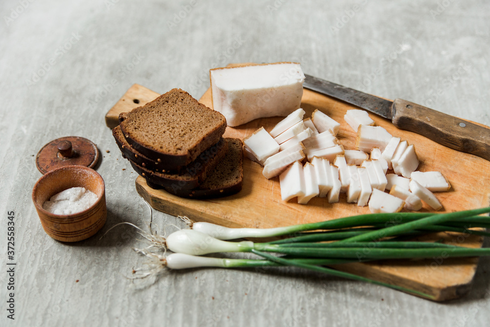 lard,bacon with black bread and green onions with salt on the wooden board. grey background. Ukrainian traditional appetizer lard,bacon with black bread and green onions with salt on the wooden board. grey background. Ukrainian traditional appetizer