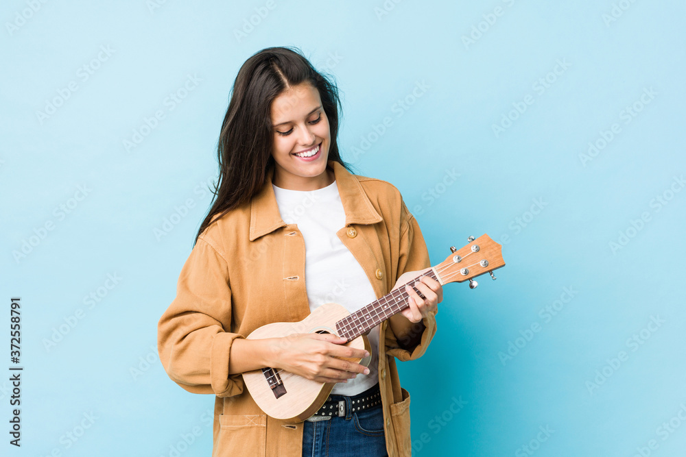 Young caucasian woman playing ukelele isolated on a blue background Young caucasian woman playing ukelele isolated on a blue background