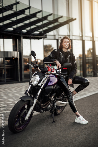 Very happy girl in a black jacket sits on a purple motorbike with a safety helmet © Fxquadro