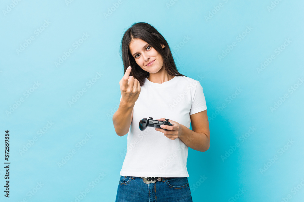 Young caucasian woman holding a game controller pointing with finger at you as if inviting come closer. Young caucasian woman holding a game controller pointing with finger at you as if inviting come closer.