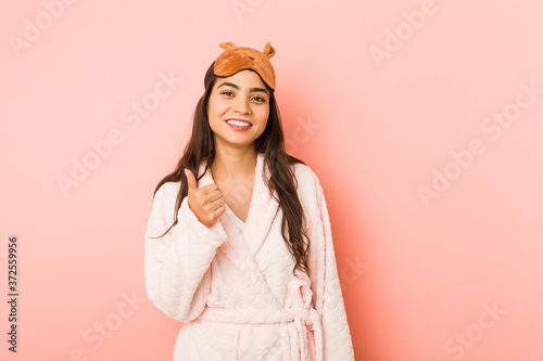 Young indian woman holding a pillow isolated smiling and raising thumb up