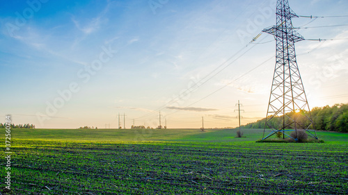 high voltage pylons at sunset with field