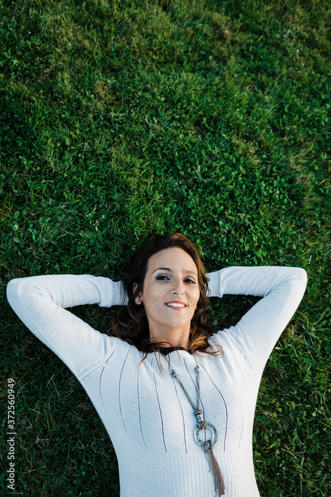 Happy mid adult woman lying on grass at park Happy mid adult woman lying on grass at park